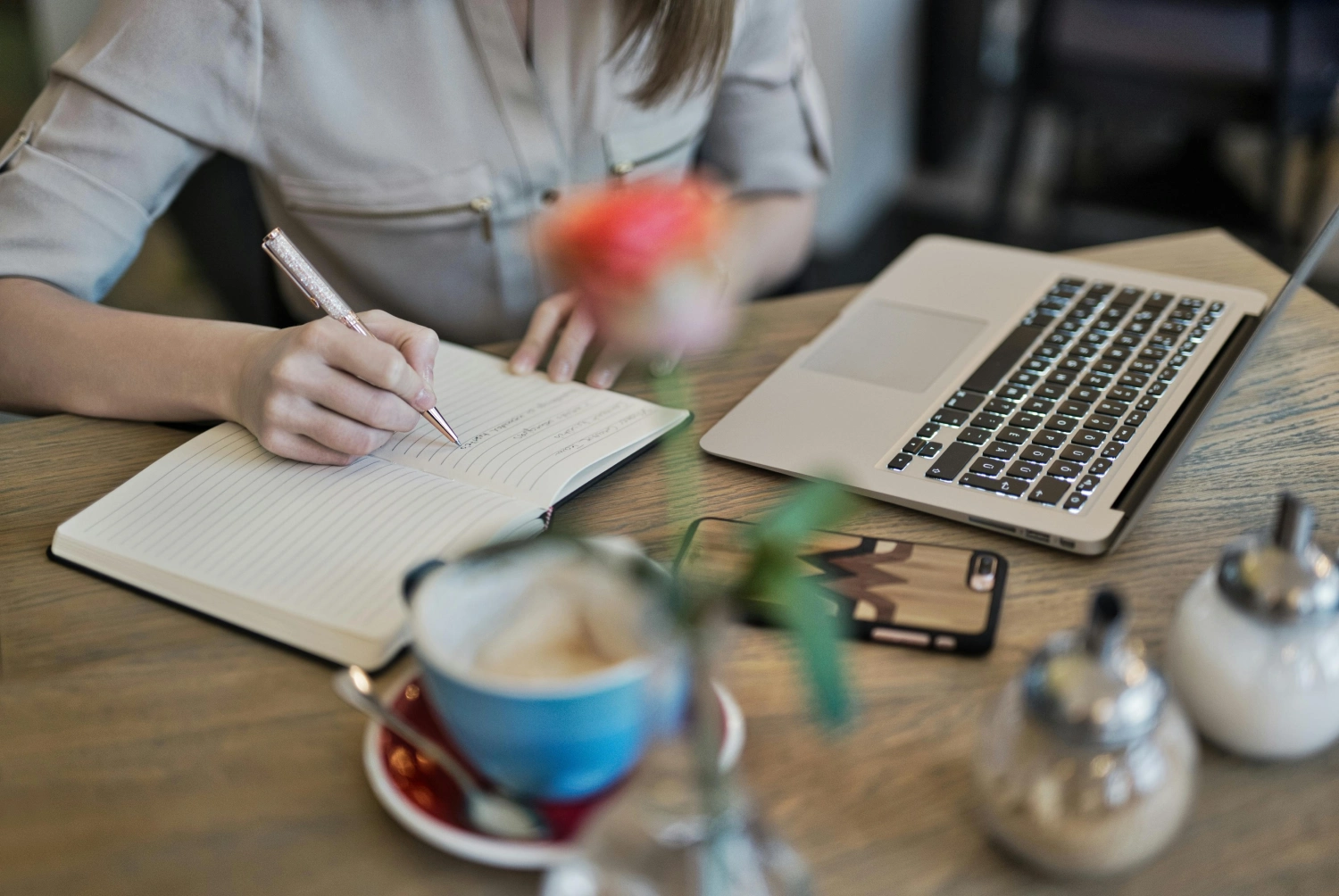 A person writing on paper at table with laptop and coffee.