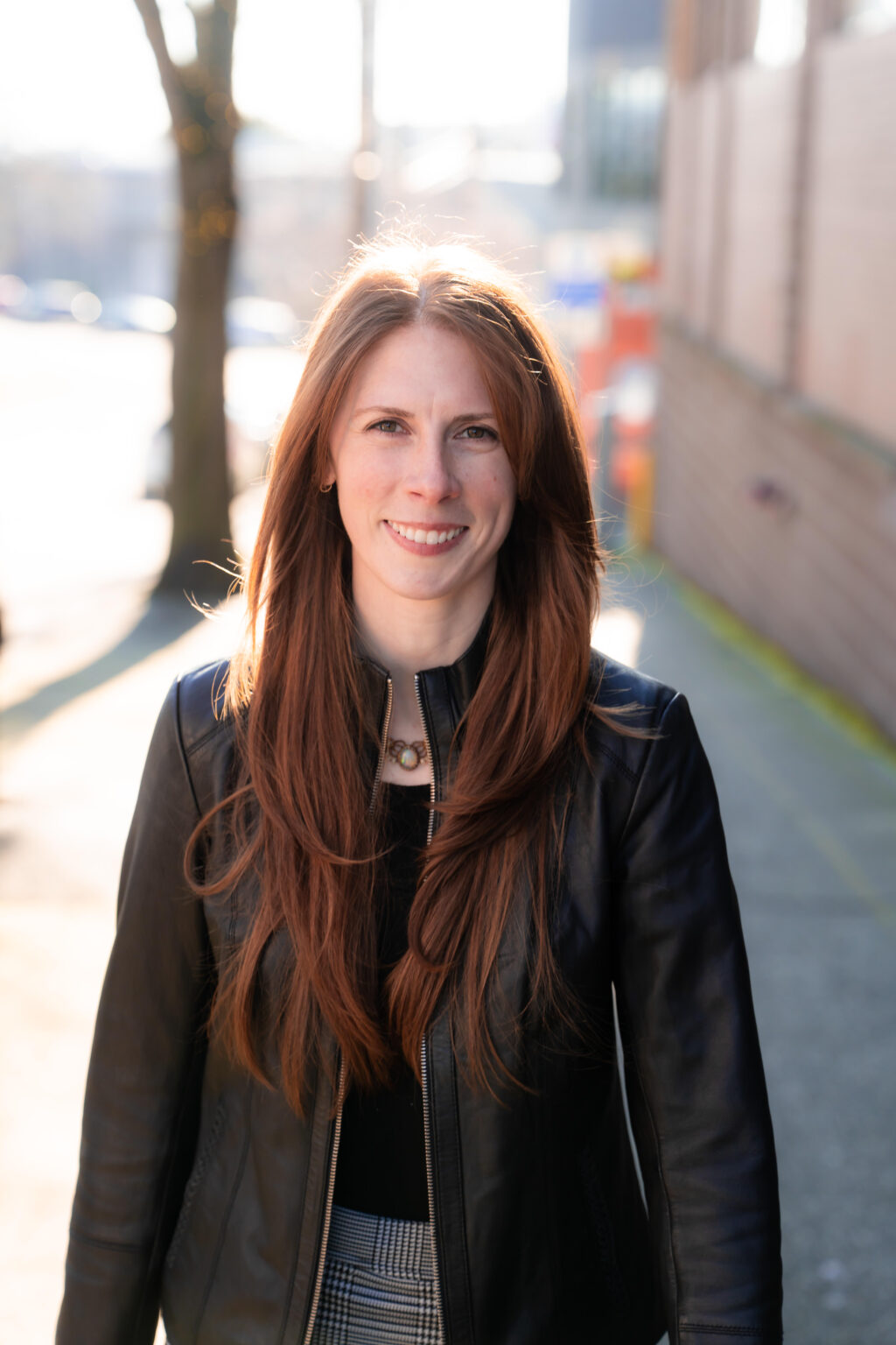 Woman smiling outdoors in sunlight.